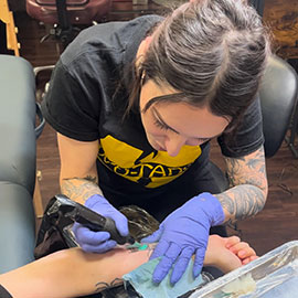 sheila.tattoos tattoos a client intently with a custom fine line design